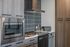 Close-up of a modern kitchen with stainless steel appliances and gray tile backsplash.