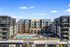 Front-facing view of The Allison apartment complex featuring a central courtyard with a resort-style pool and lounge areas, with Pottery Barn and Rejuvenation storefronts in the foreground.