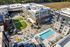 Drone shot of The Allison apartments with a pool, green lawn space, and surrounding shopping and dining areas.