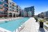 Modern rooftop pool deck with in-water lounge chairs, surrounded by apartment buildings and glass railing overlooking the city.