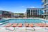 Rooftop pool with in-water loungers and a cityscape view, framed by modern buildings and clear blue skies.