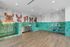 Modern pet wash station with teal tiles, stainless steel counters, a grooming table, and colorful dog mural on the wall.