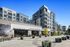 Modern mixed-use building with balconies above retail storefronts including Pottery Barn, surrounded by potted greenery and a paved walkway.