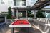Outdoor amenity area featuring a red felt billiards table under a pergola, surrounded by lounge seating, potted plants, and modern apartment architecture.