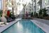 Outdoor pool area surrounded by lounge chairs, palm trees, and modern apartment buildings, creating a relaxing courtyard atmosphere.