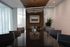 Modern conference room with a long dark table, black chairs, wood-accented ceiling, large windows with sheer curtains, and a decorative wood-paneled wall with framed artwork.