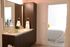 Modern bathroom featuring dark wood cabinetry, a wide vanity with a sink, large mirror, and a soaking tub with natural light streaming through a frosted window.