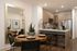 Stylish open-concept kitchen and dining area featuring a round wooden table set for four, a large wall mirror, bar seating at a kitchen island, light wood cabinetry, stainless steel appliances, and wood-style flooring.