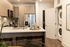 Modern kitchen with light wood cabinetry, stainless steel appliances, a large island with bar seating, and a stacked washer and dryer visible through an open door to the side.