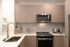 Contemporary kitchen with stainless steel appliances, including a microwave and gas range, light wood cabinetry, a deep sink, and a white tile backsplash.