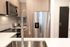 Close-up view of a modern kitchen featuring a double-basin stainless steel sink, stainless steel refrigerator, microwave, light wood cabinetry, and white quartz countertops.