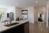 Modern apartment interior featuring an open-concept kitchen with stainless steel sink and faucet, light cabinetry, wood-style floors, and a glimpse into the living and bedroom areas.