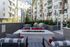 Spacious outdoor courtyard with cushioned seating, red accent pillows, and a large square fire pit, surrounded by apartment balconies and tall palm trees.