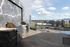 Rooftop grilling area with a built-in stainless steel barbecue station, modern patio furniture, and panoramic views of the city and surrounding hills.
