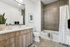 A bright, modern bathroom featuring a large mirror above a double vanity with wooden cabinetry, a toilet, and a tiled bathtub with a white shower curtain, all accented by clean lines and neutral tones.