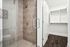 A contemporary bathroom with a glass-enclosed shower featuring tile walls and flooring, a white vanity with a wide countertop and storage drawers, and dark wood flooring that adds contrast to the clean, modern design.