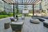 Modern outdoor lounge area with cushioned seating, a pergola overhead, and a large screen for outdoor movies, surrounded by apartment buildings and greenery.
