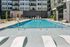 Large outdoor swimming pool surrounded by lounge chairs, red umbrellas, and modern apartment buildings.