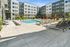 Wide view of a pool area with lounge chairs, red umbrellas, and landscaped surroundings, set within a modern apartment courtyard.