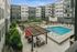 Courtyard view of a pool area with lounge chairs, a shaded pergola seating area, red umbrellas, and modern apartment buildings surrounding the space.