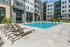 Outdoor pool area featuring multiple lounge chairs arranged along the pool deck, surrounded by modern apartment buildings.