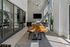 Modern meeting or work area with a long wooden table, chairs, large TV, and floor-to-ceiling windows letting in abundant natural light.
