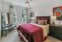 Cozy bedroom with a deep red bedspread, upholstered headboard, large windows, modern furniture, and decorative artwork.