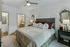 Bright, modern bedroom with a large upholstered bed, nightstands, a ceiling fan, and direct access to an ensuite bathroom and walk-in closet.