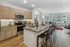 Modern kitchen with wood cabinetry, stainless steel appliances, a granite island with barstool seating, and an open view into the adjacent dining and living areas.