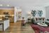 Open living space with a contemporary kitchen, a seating area with a sofa and coffee table, large artwork on the wall, and wood flooring throughout.
