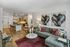 Open-concept living room with a sectional sofa, red accent rug, wall art, and a view into a modern kitchen and dining area.