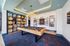 A contemporary lounge with a centrally positioned pool table, high ceilings with recessed lighting, a patterned carpeted floor, built-in shelving filled with books and d&eacute;cor, and framed artwork on the walls, all creating an upscale, relaxed atmosphere.