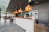 A modern resident lounge featuring a long white bar with a wooden top, pendant lighting, blue bar stools, and gray tiled flooring, with a seating area and large windows in the background that add natural light and warmth to the stylish setting.