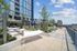 A rooftop terrace with white hammocks strung between poles, surrounded by greenery in raised concrete planters, tiled flooring, string lights, and views of nearby high-rise buildings under a partly cloudy sky.