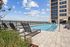 Rooftop pool with lounge chairs and city skyline views under a partly cloudy sky.