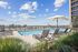 Stylish rooftop pool with designer lounge chairs, shaded umbrellas, and sweeping skyline views under a vibrant blue sky.