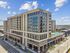 Modern mid-rise apartment building with expansive glass windows, street-level retail, and elevated rooftop amenities, set against a bright blue sky.