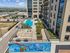 Bird&rsquo;s-eye view of a resort-style rooftop pool and sundeck, complete with lounge seating, umbrellas, and lush landscaping, surrounded by modern high-rise architecture.