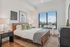 Stylish bedroom with a large window, cozy bed with throw pillows and blankets, nightstands, wall art, and a patterned area rug.