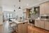Contemporary kitchen with light wood cabinetry, stainless steel appliances, a large island with seating, pendant lighting, and an adjacent dining area.