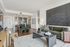 Open-concept living and kitchen area in a modern apartment featuring a green velvet sofa, large chalkboard-style artwork, dark wood coffee table, and a sleek kitchen with bar seating and pendant lighting.
