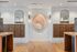 Stylish apartment mailroom with symmetrical wooden mail cabinets, decorative wall sconces, arched mirrors, and a central abstract art piece above a white wall.