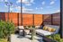 Outdoor rooftop lounge area with a cushioned sectional sofa, throw pillows, greenery, and modern patio furniture under a bright blue sky.