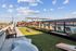 Rooftop amenity space featuring a cornhole lawn game area, wooden benches, shaded lounge seating, and poolside chairs with a city view backdrop.