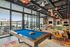 Modern resident lounge featuring a billiards table, cozy seating areas, pendant lighting, and floor-to-ceiling windows overlooking a pool deck.