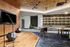 Contemporary lounge with a small stage and microphones, plush green bench seating, gold ceiling tiles, black geometric stools, and a built-in bar wall with golden jars.