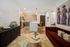 Contemporary open-plan living room and kitchen with modern furniture, a white table lamp in the foreground, a red velvet sofa, and patterned rug.