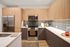 Modern U-shaped kitchen with stainless steel refrigerator, black oven, and wood-grain cabinetry paired with white countertops and a tiled backsplash.