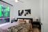 A modern bedroom featuring a large window with natural light, a bed with soft mauve bedding, a faux fur throw, abstract wall art, and sleek black nightstands with matching lamps.