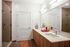 A well-lit bathroom featuring a large vanity with wood cabinetry, double sinks, a wide mirror with overhead lighting, and a white shower and tub combo.